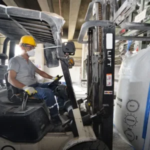 Forklift driver wearing protective mask while moving a bulk bag